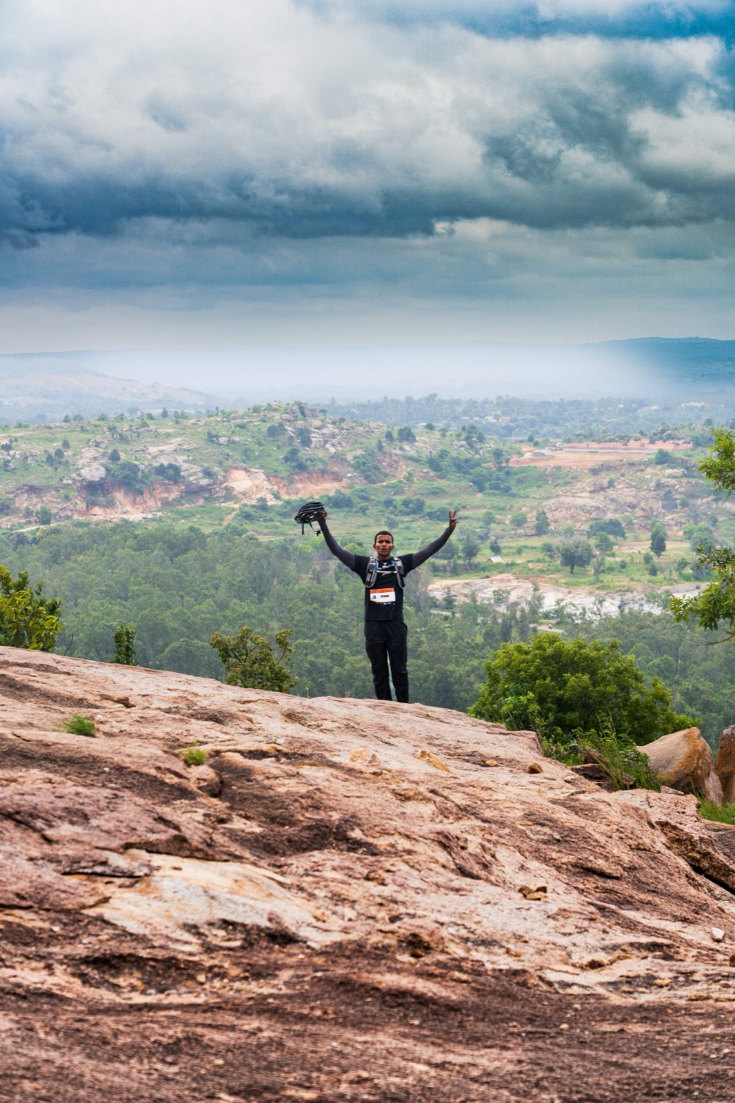A racer on a summit rock with arms thrown open, looking out over a wide valley