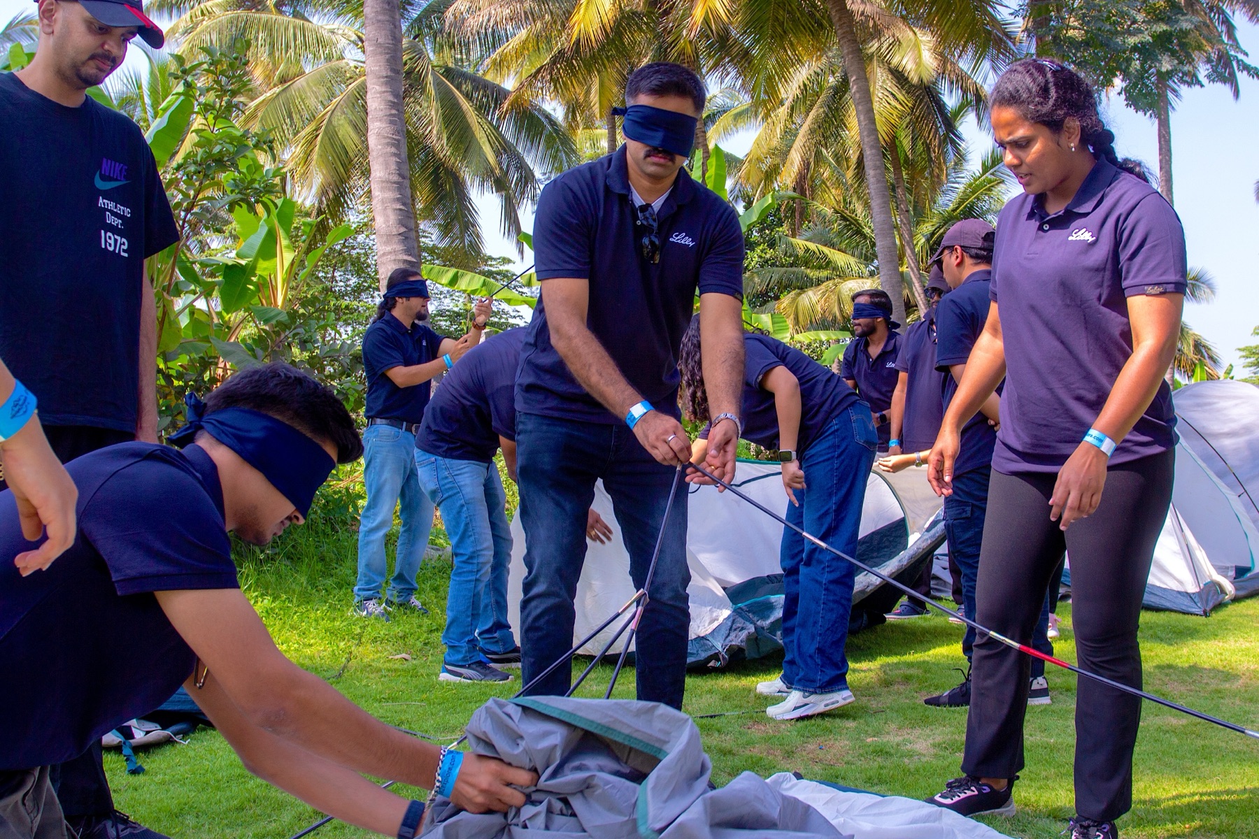Blindfolded team members pitching a tent together while a colleague guides them